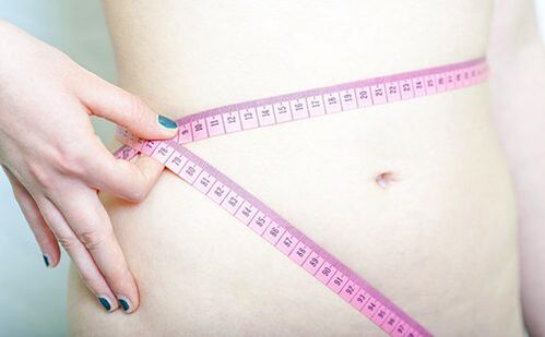 Bir kız Dukan diyetinin sonuçlarını kaydetmek için belini ölçüyor